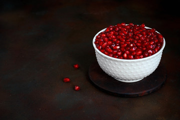 Pomegranate seeds in a bowl on black background.