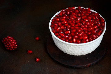 Pomegranate seeds in a bowl on black background.