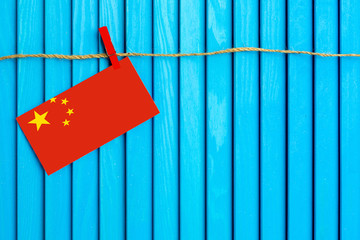 Flag of China hanging on clothesline attached with wooden clothespins on aqua blue wooden background. National day concept.