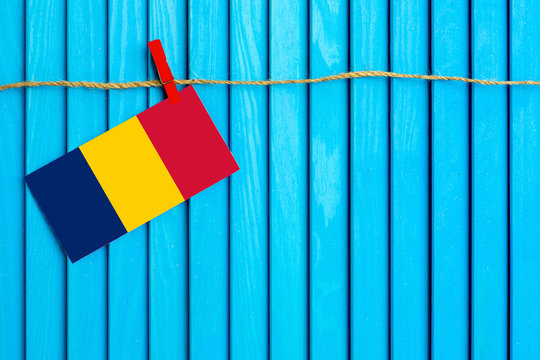 Flag of Chad hanging on clothesline attached with wooden clothespins on aqua blue wooden background. National day concept.