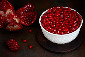 Pomegranate seeds in a bowl on black background.