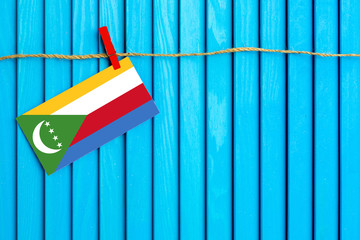 Flag of Comoros hanging on clothesline attached with wooden clothespins on aqua blue wooden background. National day concept.