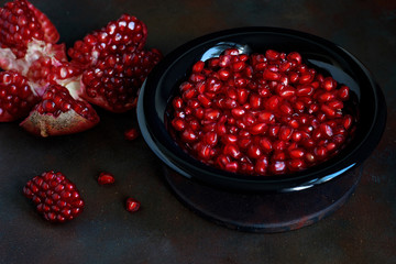 Pomegranate seeds in a bowl on black background.