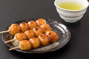 黒い背景にタレがたっぷりついたみたらし団子とお茶日本のデザート和菓子