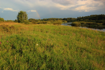 Summer evening after rain, rainbow in the sky, view of the riverbed from the high bank.