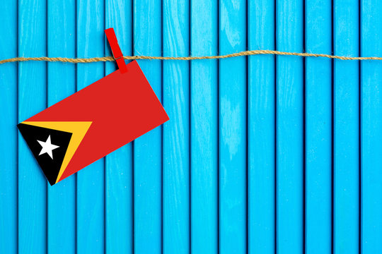 Flag of East Timor hanging on clothesline attached with wooden clothespins on aqua blue wooden background. National day concept.