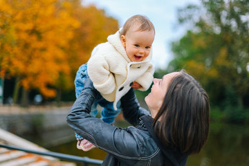 Mother playing and having fun with her little kid in sunshine, warm autumn park. Happy parent and...