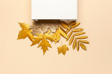 Flat lay creative autumn composition. White Gift Paper package and Golden leaves on beige background top view copy space. Fall concept. Autumn background. Minimal concept idea, floral design