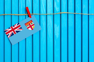 Flag of Fiji hanging on clothesline attached with wooden clothespins on aqua blue wooden background. National day concept.
