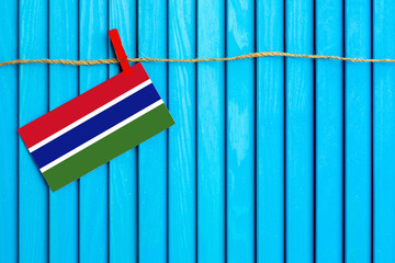 Flag of Gambia hanging on clothesline attached with wooden clothespins on aqua blue wooden background. National day concept.