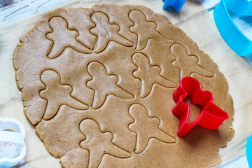 process of dealing with gingerbread man cookies,use red gingerbread man  mold cutting gingerbread dough on baking paper around colorful cookie cutters on white wooden table.top view
