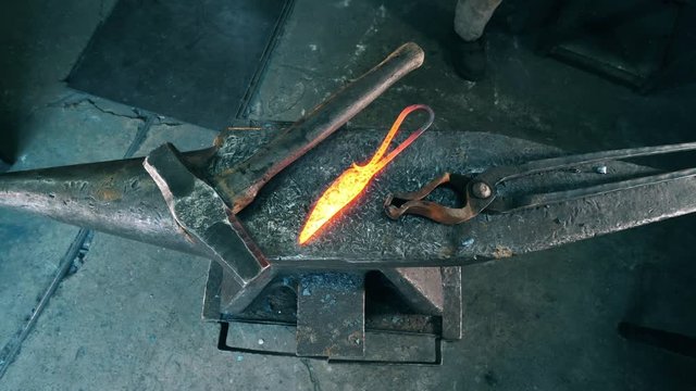 Professional blacksmith puts hot knife on anvil at a forge.