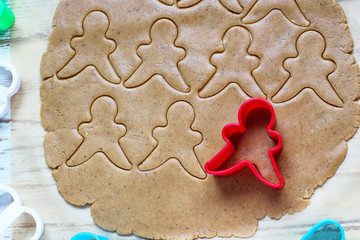 process of dealing with gingerbread man cookies,use red gingerbread man  mold cutting gingerbread dough on baking paper around colorful cookie cutters on white wooden table.top view