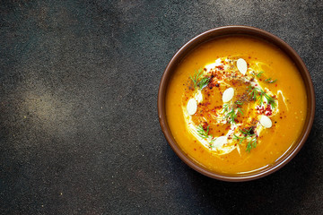 Roasted pumpkin and carrot soup with cream, seeds and fresh green in ceramic bowl on grunge black background. Top view.Spaces for text and copy