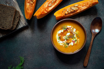 Roasted pumpkin and carrot soup with cream, seeds and fresh green in ceramic bowl on grunge black background. Top view.Spaces for text and copy