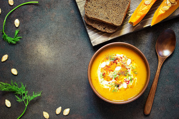 Roasted pumpkin and carrot soup with cream, seeds and fresh green in ceramic bowl on grunge black background. Top view.Spaces for text and copy