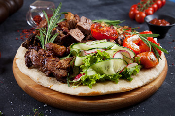 Close up view on tasty grilled meat with vegetables on georgian pita. shashlik or barbecue meat on pita. Shish kebab, traditional georgian cuisine food. Copy space for design. Dark background