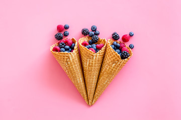 Fresh berries in waffle cones on pink background top view