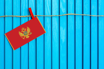 Flag of Montenegro hanging on clothesline attached with wooden clothespins on aqua blue wooden background. National day concept.