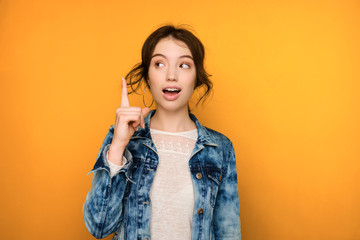 A dark-haired girl in jeans stands on a yellow background and enthusiastically looking to the side,...