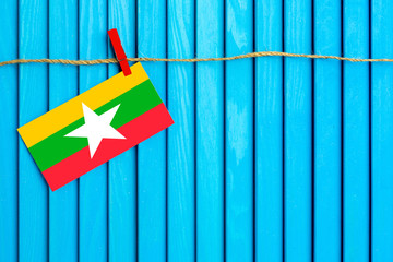 Flag of Myanmar hanging on clothesline attached with wooden clothespins on aqua blue wooden background. National day concept.