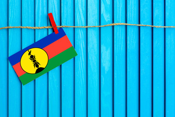 Flag of New Caledonia hanging on clothesline attached with wooden clothespins on aqua blue wooden background. National day concept.