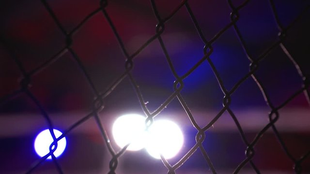 Fence of MMA boxing ring grill with color lights in the background with bokeh, Martial Arts close up