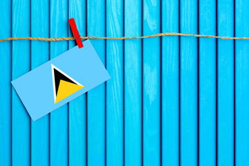 Flag of Saint Lucia hanging on clothesline attached with wooden clothespins on aqua blue wooden background. National day concept.