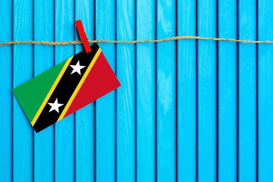 Flag of Saint Kitts And Nevis hanging on clothesline attached with wooden clothespins on aqua blue wooden background. National day concept.