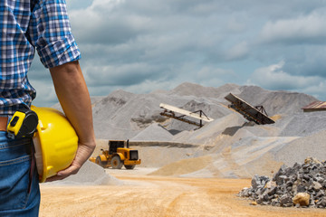 Engineer holding a yellow helmet for the safety of workers on a background of coal mining trucks...