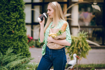 Fototapeta premium Beautiful blonde girl holds package with food in her hands. Beautiful blonde drinking coffee.