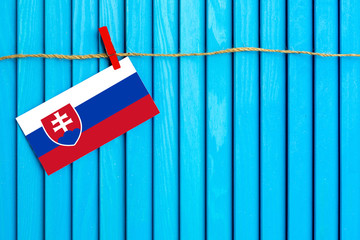 Flag of Slovakia hanging on clothesline attached with wooden clothespins on aqua blue wooden background. National day concept.
