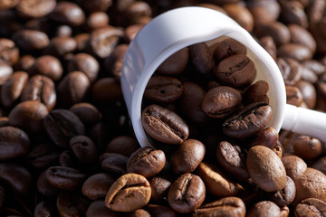 white ceramic measuring spoon and coffee beans, roasted coffee. close up