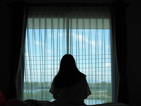 silhouette of alone woman sitting on the bed beside the windows with sunlight in the morning 