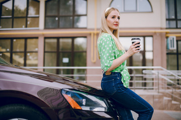 Beautiful blonde girl sitting in the car driving listening to music and drinking coffee