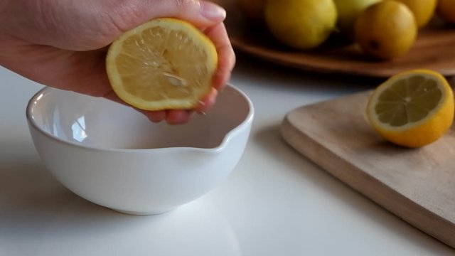 Squeezing fresh lemon juice by hand into white ceramic spouted bowl, letting pips and seeds fall in. close up.