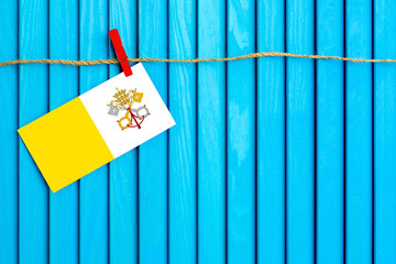 Flag of Vatican City hanging on clothesline attached with wooden clothespins on aqua blue wooden background. National day concept.