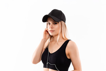 Young sporty blond woman in a black sportswear with smart watches listens to music during workout standing over white background.