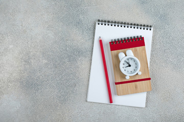 Back to school. School time minimal concept. Notepad, pencil, alarm clock on grey concrete background. Flat lay, top view