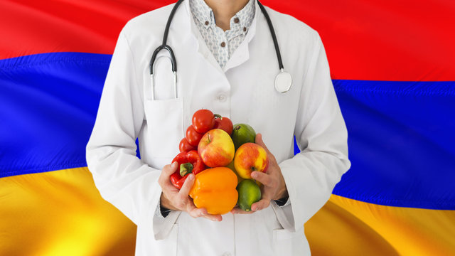 Armenian Doctor Is Holding Fruits And Vegetables In Hands With Armenia Flag Background. National Healthcare Concept, Medical Theme.