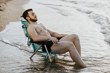 relaxed bodybuilder man in a beach chair on the shore