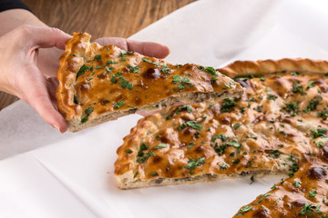 Female hand holding slice of homemade pie stuffed with potato and mushrooms