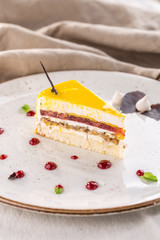 A piece of mousse cake with mango and strawberry on a white plate on tablecloth