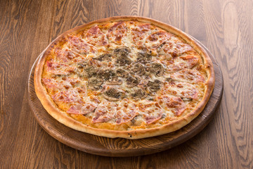 Italian Pizza with ham, sliced mushrooms, tomato sauce and cheddar isolated on wooden background