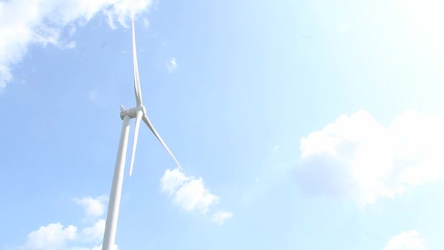 Windmill energy generator against a blue sky with white clouds - aligned left