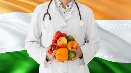 Doctor is holding fruits and vegetables in hands with India flag background. National healthcare concept, medical theme.
