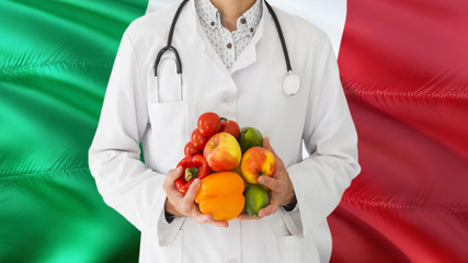Doctor is holding fruits and vegetables in hands with Italy flag background. National healthcare concept, medical theme.