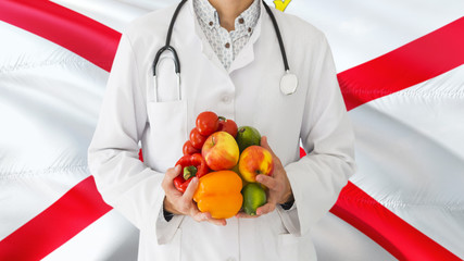 Doctor is holding fruits and vegetables in hands with Jersey flag background. National healthcare concept, medical theme.