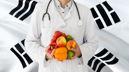 Doctor is holding fruits and vegetables in hands with South Korea flag background. National healthcare concept, medical theme.