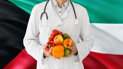 Doctor is holding fruits and vegetables in hands with Kuwait flag background. National healthcare concept, medical theme.